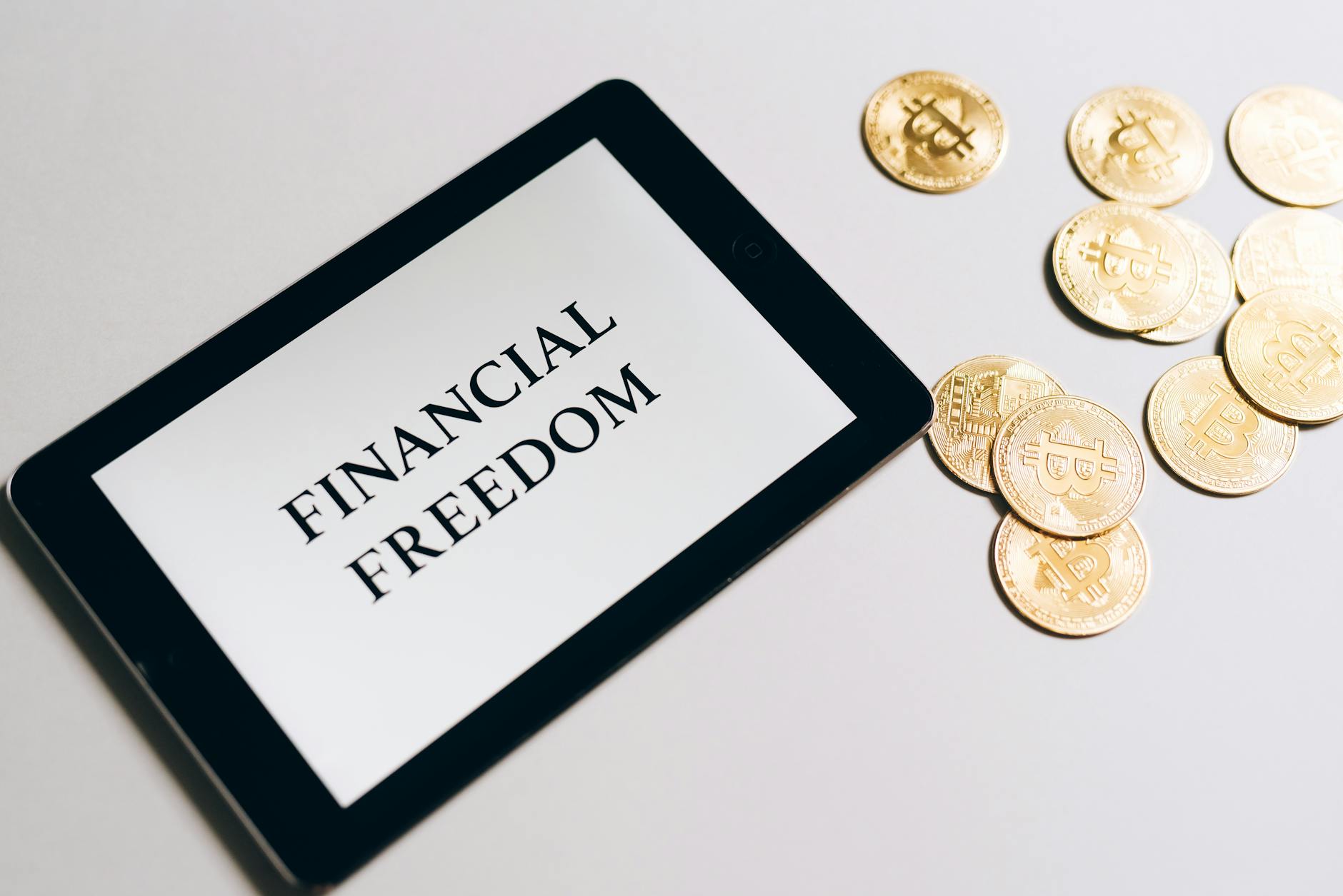 tablet showing 'financial freedom' with gold bitcoins nearby, symbolizing cryptocurrency investment showing how to protect assets strategy for high-net-worth individuals considering irrevocable trust asset protection